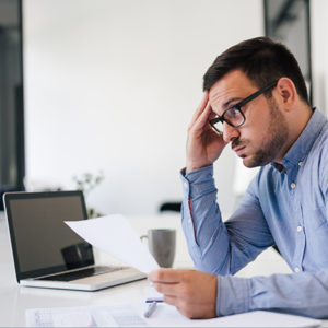 Man concerned, sitting at computer with papers #2