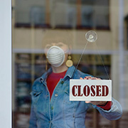 Woman with a face mask placing a closed sign on shop door
